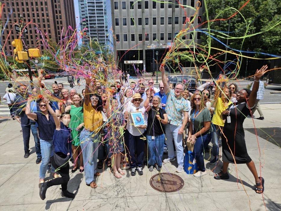 Celebratory group photo outside of One Parkway Building. The group has their hands in the air and tosses confetti