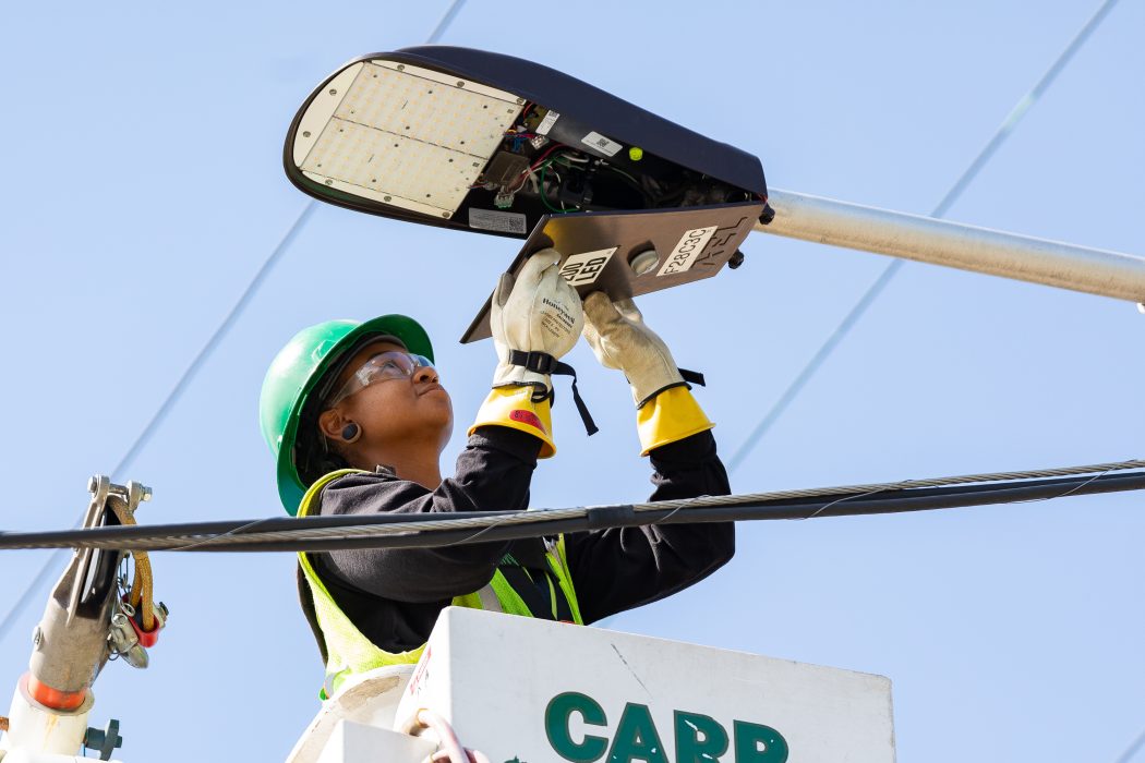 A person installing a new LED bulb into a City-owned streetlight.