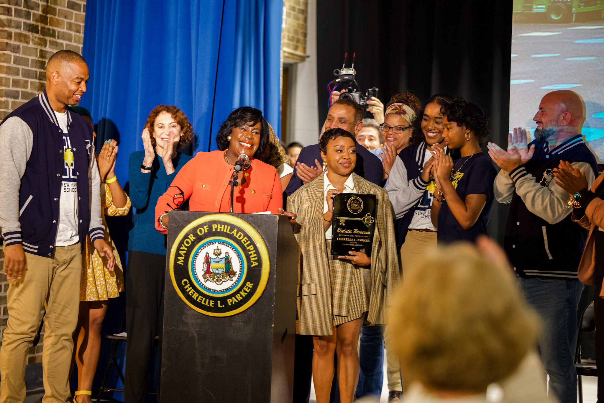 Mayor Cherelle Parker is on stage and presenting actress Quinta Brunson with a ceremonial key to the city. Behind them there are people cheering and clapping.