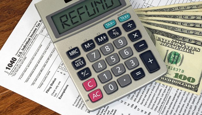 Picture showing a 1040 federal tax return form, hundred-dollar bills and a calculator