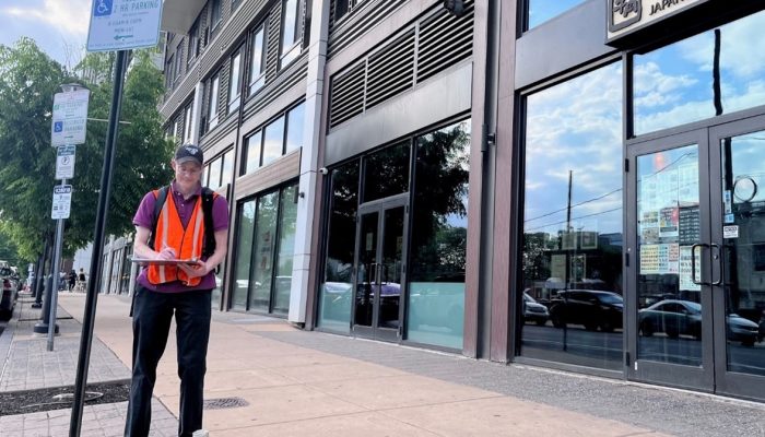 A city planner wearing a hi-viz vest stands outside a building and records data onto a clip board.