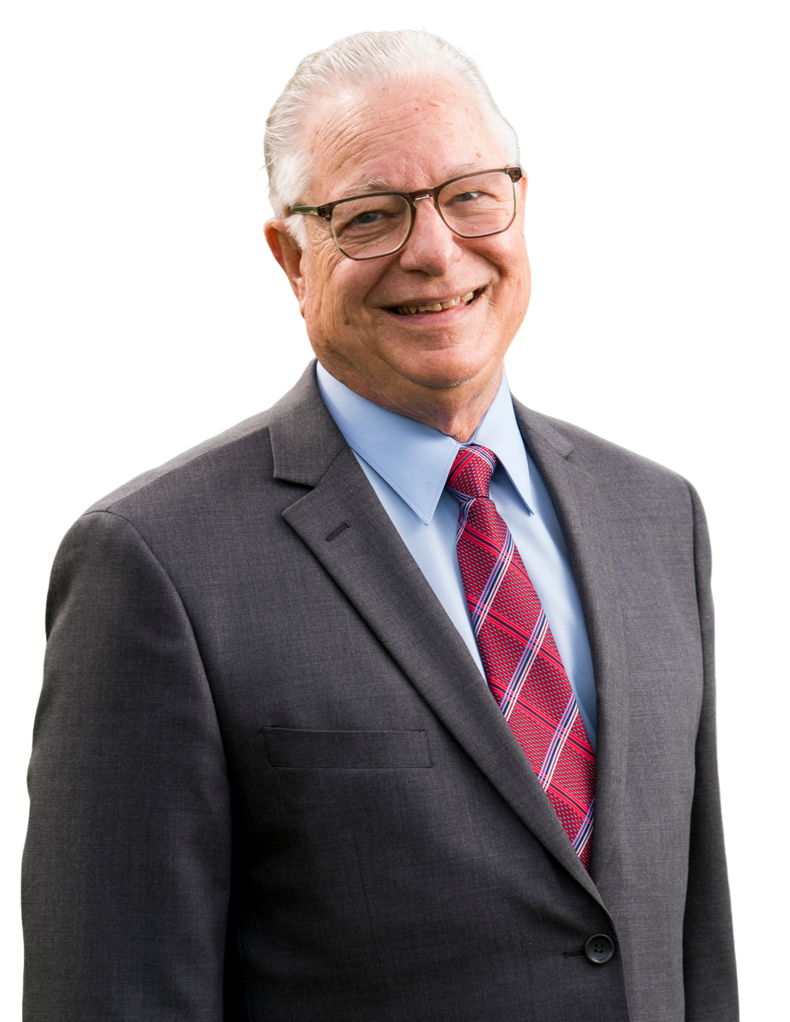 A man in a blue buttoned shirt, red striped tie and gray blazer smiling and wearing black framed glasses.
