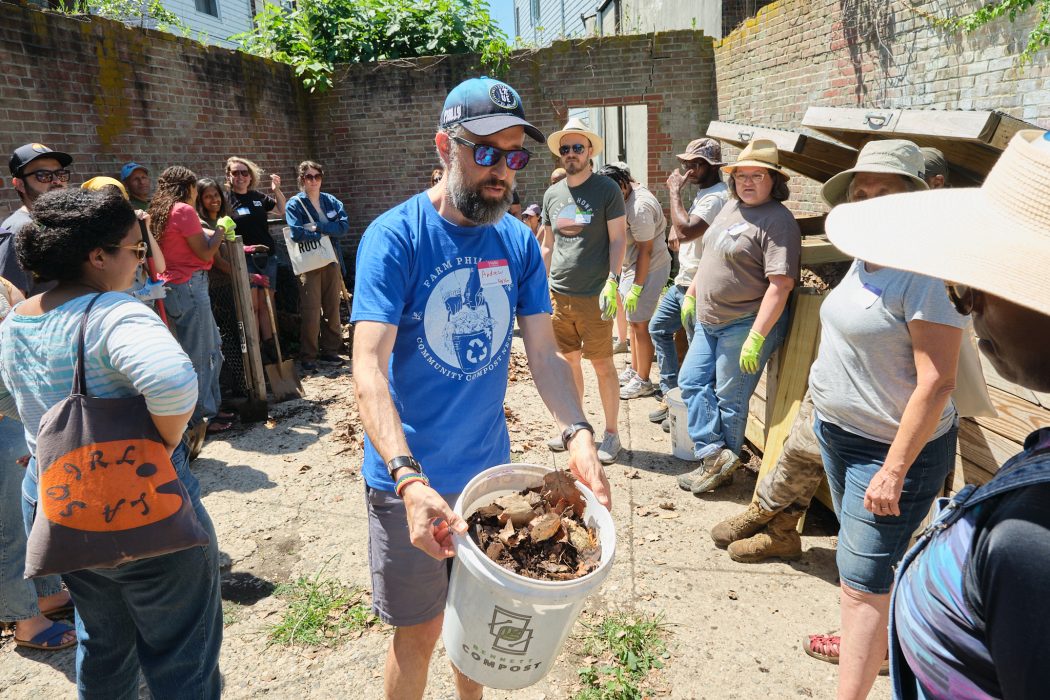 A crowd of people gather around a bucket of compost at a Farm Philly demonstration.