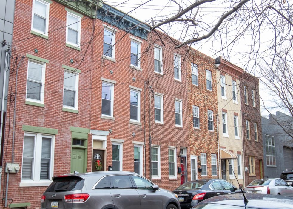 Rowhouses in a Philadelphia neighborhood with cars parked out in front.