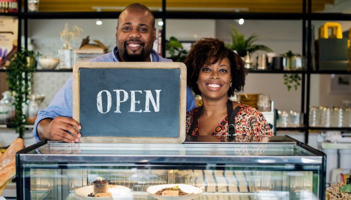 A smiling couple hold Open sign