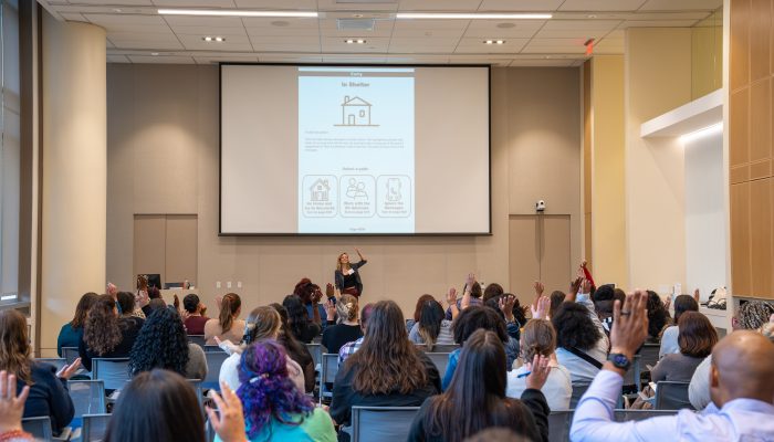 Attendees at the Safer Futures Conference participate in an interactive session, raising their hands.