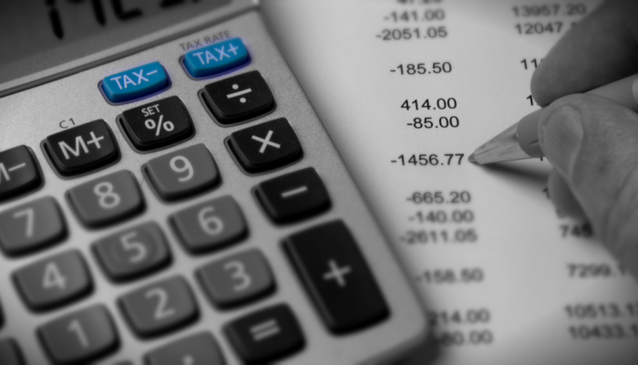 A hand holding a pen next to a calculator 