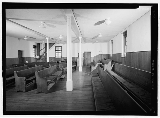 A black and white, historical photo of the interior of the Friends meeting house. There are pews arranged so that congregants face each other.