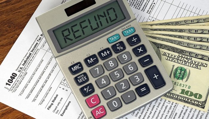 A calculator with the word REFUND on it, a 1040 tax form, and a stash of $100 bills