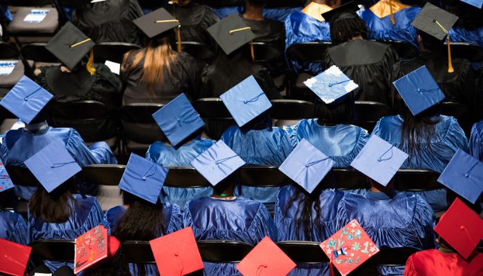 Birdseye view of students during graduation, wearing graduation caps and gowns in various colors.