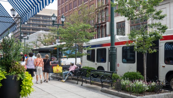Photo of the 800 block of Market Street, in the summertime. A fabric awning stretches over the sidewalk and a pedestrian rests on a bench surrounded by planters. On the street, a SEPTA bus kneels for passengers.