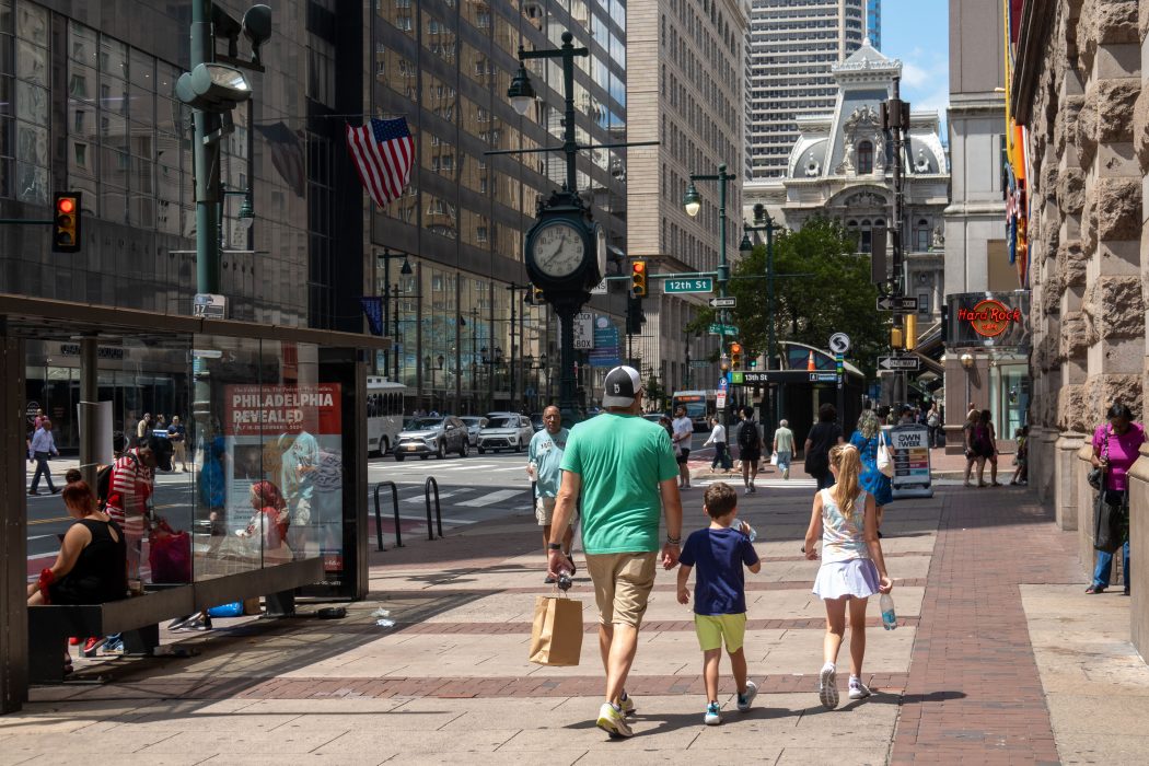 A photo of summertime on Market Street, near 12th and Market. Pedestrians stroll with a shopping bag in hand.