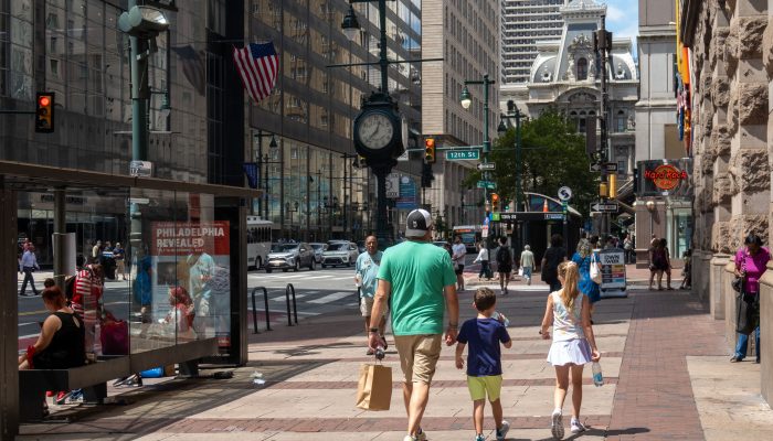 A photo of summertime on Market Street, near 12th and Market. Pedestrians stroll with a shopping bag in hand.