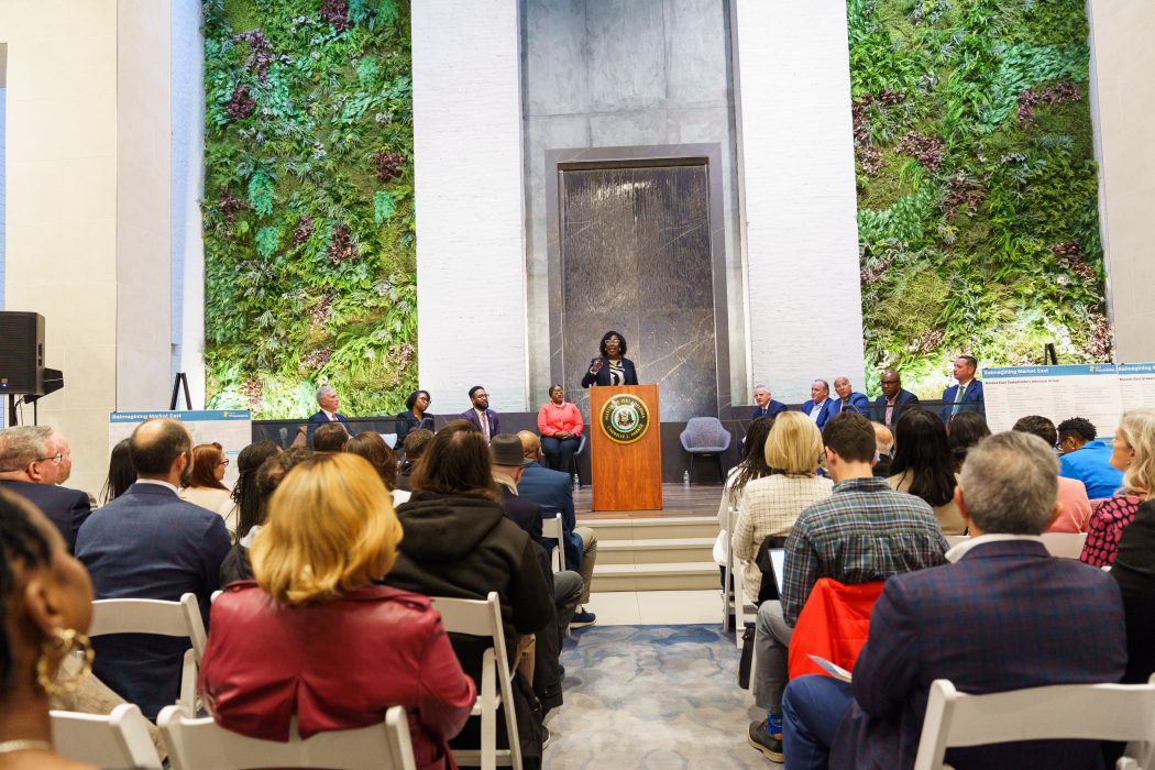 Mayor Cherelle L Parker stands at a podium to address a seated crowd gathered inside the Jefferson lobby at 1100 Market Street.