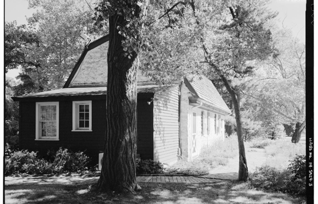 Black and white photo of a stone cottage with a small shed addition