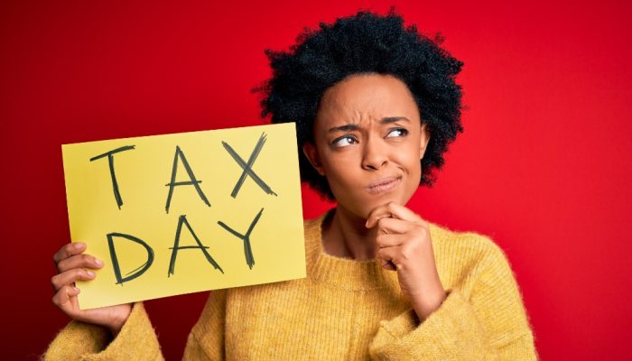 Woman holds up a yellow poster with Tax Day written on it