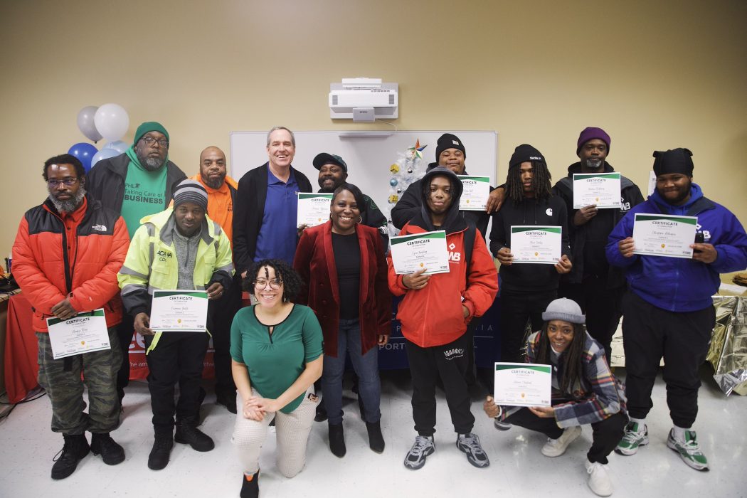 Graduates from the Taking Care of Business Program smile holding their training graduation certificates with Taking Care of Business Program staff at a recent graduation ceremony