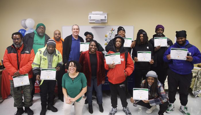 Graduates from the Taking Care of Business Program smile holding their training graduation certificates with Taking Care of Business Program staff at a recent graduation ceremony