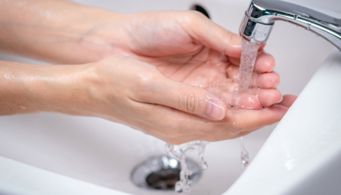 Person washes their hands while water flows through bathroom sink