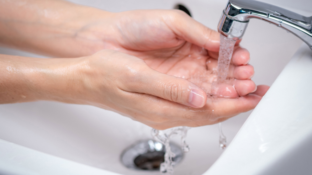 Person washes their hands while water flows through bathroom sink