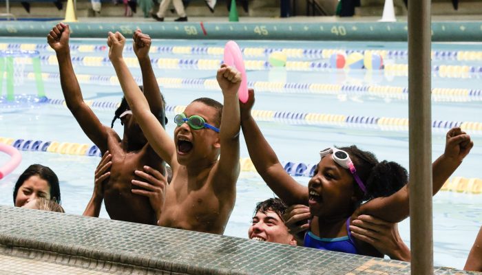 Children are gathered at the side of a pool cheering.