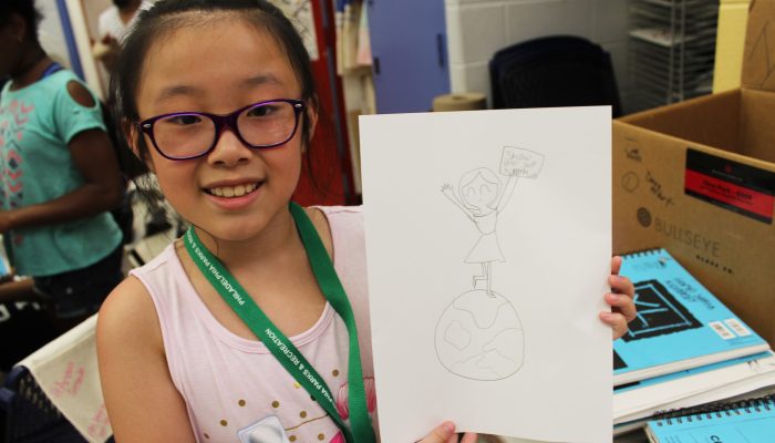 A young child smiles and holds up their drawing.