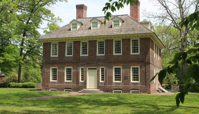 A two-and-a-half story brick building with light trim and wood-shake roof. Purple flowers appear in the foreground.