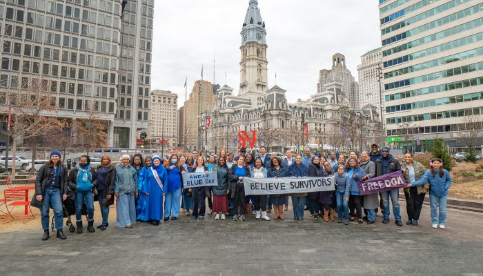 A group of advocates wearing blue stand in Love Park holding banners that say "Believe Survivors," "Wear Blue Day" and "Freedom" for Human Trafficking Awareness Day