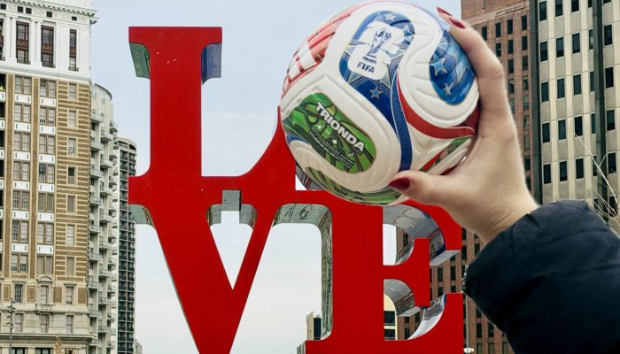 A hand holding a FIFA World Cup ball over the O in the Love Park statue in Center City Philadelphia