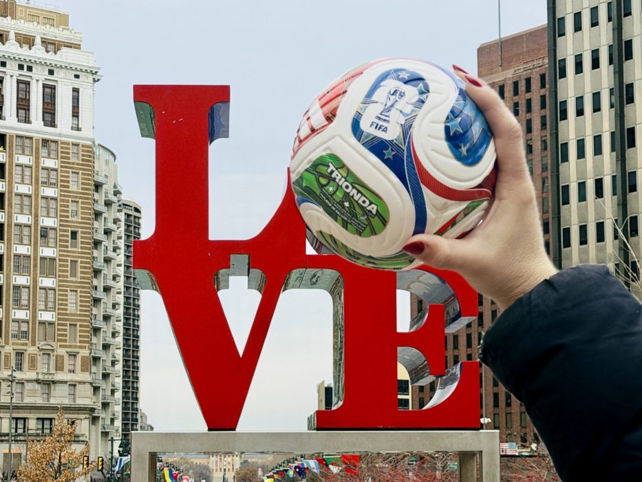 A hand holding a FIFA World Cup ball over the O in the Love Park statue in Center City Philadelphia
