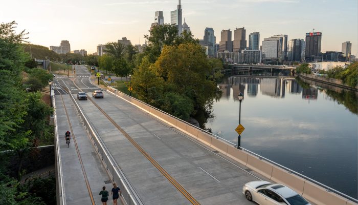 Un automóvil circulando por la autopista junto a un río, con el horizonte de Filadelfia de fondo.
