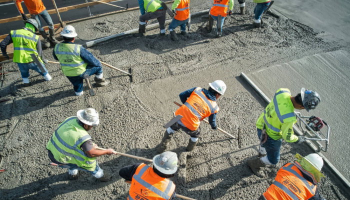 Construction workers smoothing and leveling concrete at an elevated level of a new apartment building complex development.