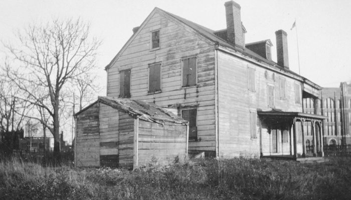 An old, black and white photo of a farmhouse surrounded by tall grass.