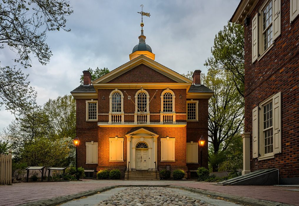 A Colonial-era brick building with a weathervane on top.