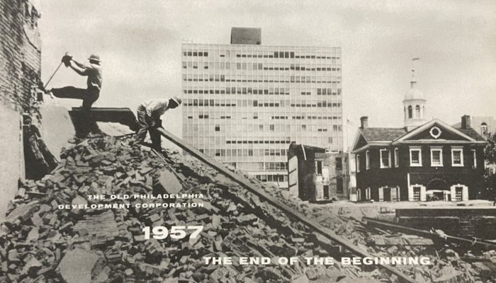A black and white photo of two men in hard hats standing atop a pile of construction rubble. In the background is Carpenters' Hall. Text in image says the old philadelphia development corporation 1957 the end of the beginning.