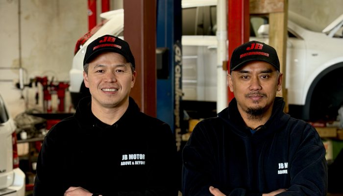JB Motor Works’ co-founder, John Lin and his business partner Bruce together at the business with a car on a lift in the background.