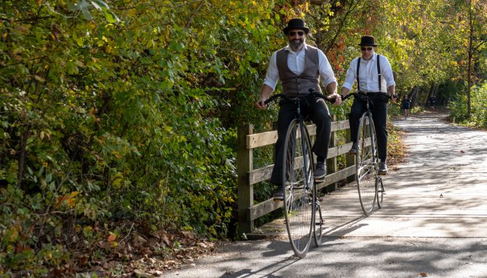 Two cyclists riding penny farthing bicycles on the Manayunk Canal Towpath.