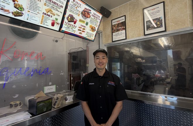 Business owner stands inside in front of counter and menu at Korea Taqueria