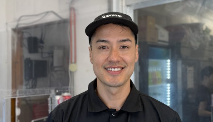 Business owner standing inside in front of the counter and menu at Korea Taqueria