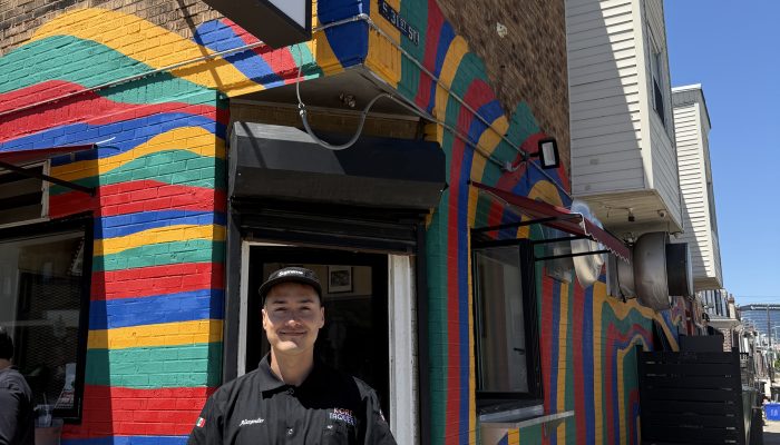 Business owner stands outside at Korea Taqueria with the colorfully painted exterior of the business in the background