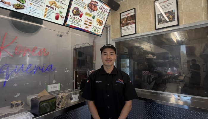 Business owner standing inside Korea Taqueria in front of counter with menu in background