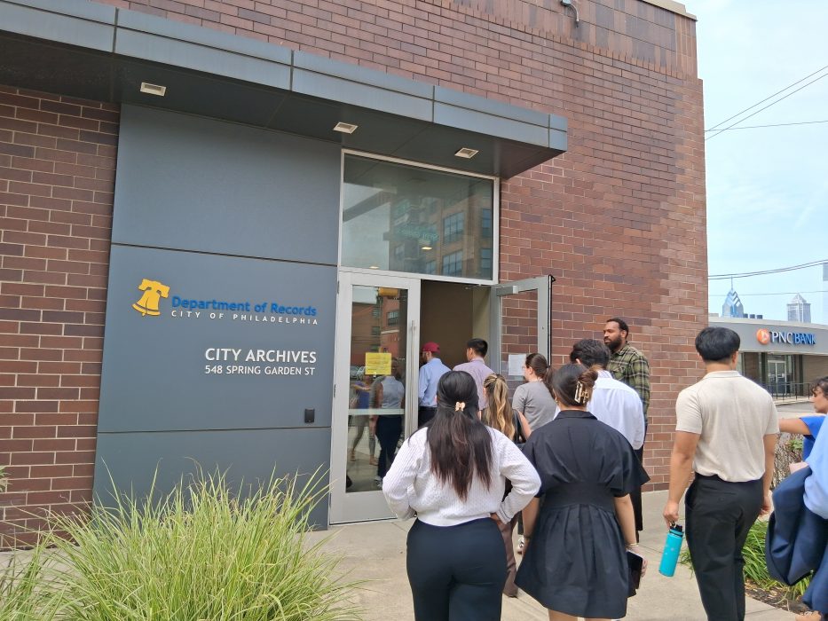 A group of interns walk into a building past the entrance that says "Department of Records, City Archives, 548 Spring Garden St"