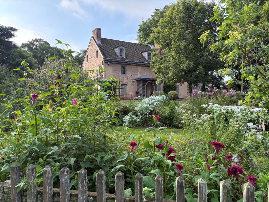 Photo of a flower garden with a three-story stone house in the distance.