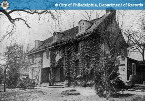 Historical photo of a three-story stone house with ivy growing across the front facade.