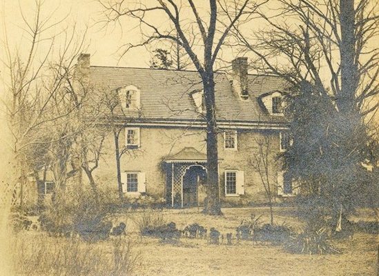 Historical photo of a three-story stone house with a semi enclosed porch made of lattice.