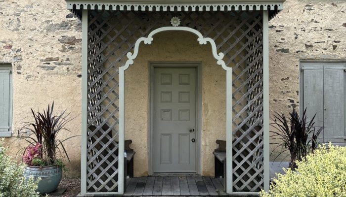 Photo of front door to the stone house. There is a semi enclosed porch made of lattice work.