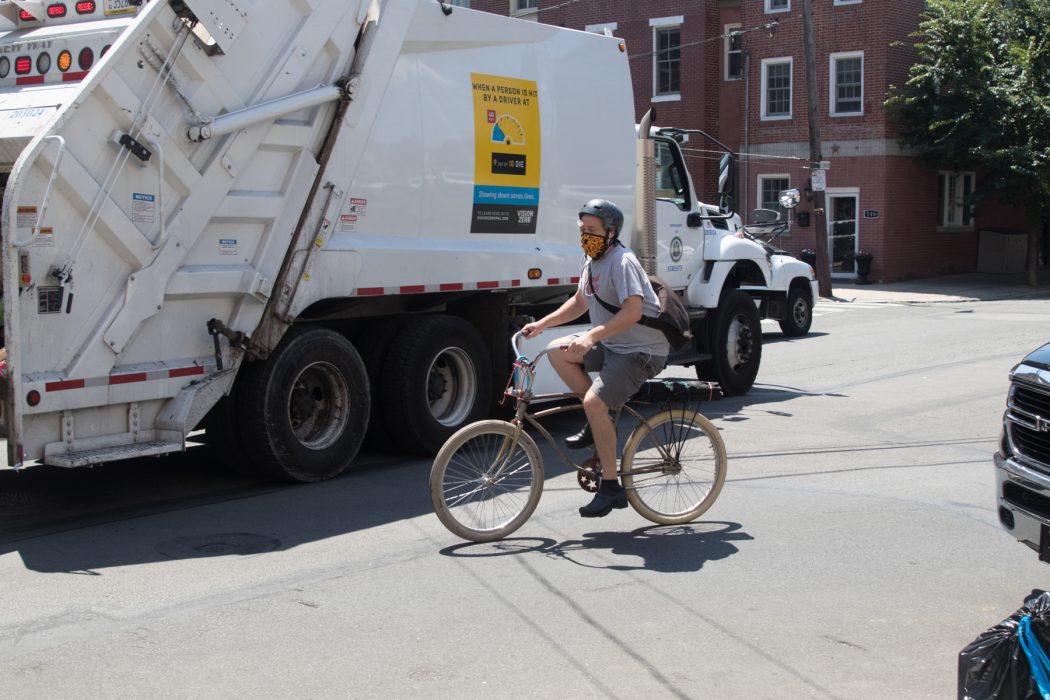 A person on a bike riding by a trash truck on the street.