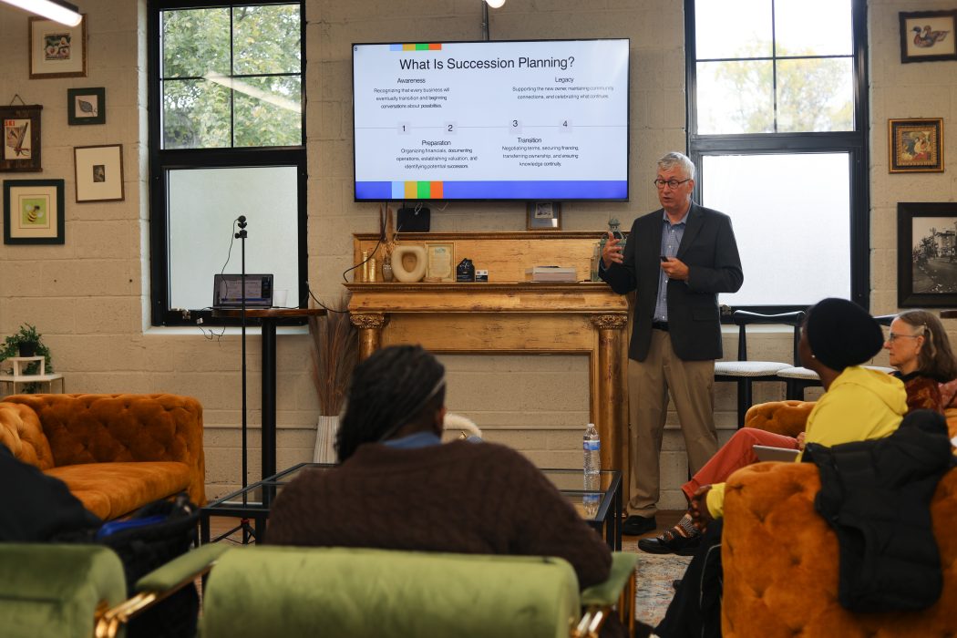 A presenter stands in front of a classroom for a succession planning session with a screen behind him showing a slide that says, "What is succession planning?"