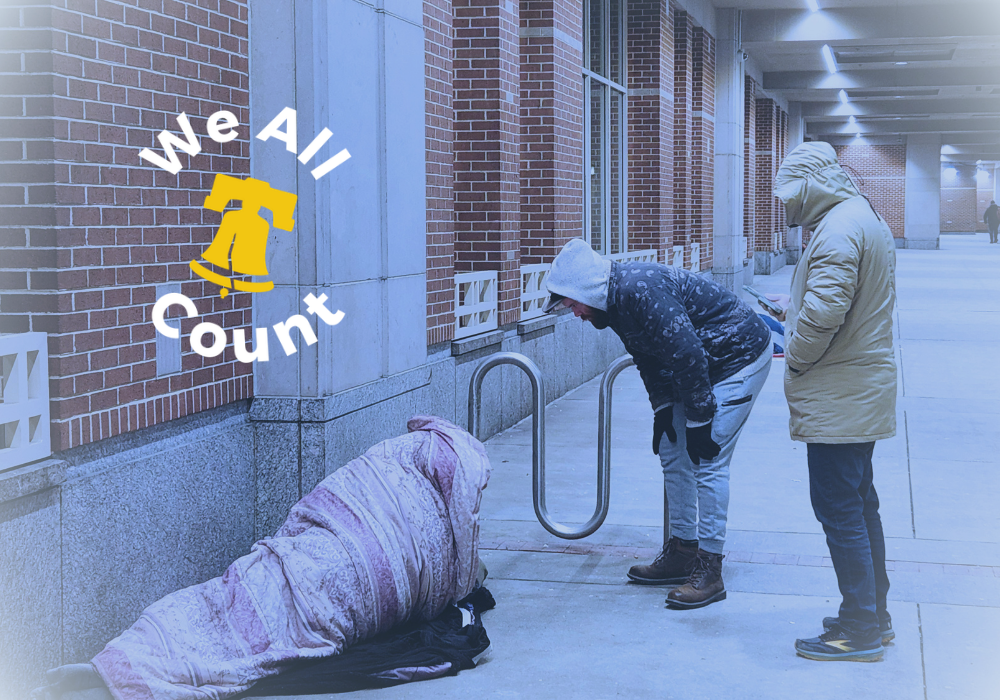 Two volunteers help someone sleeping on the sidewalk in the winter wrapped in a quilt.