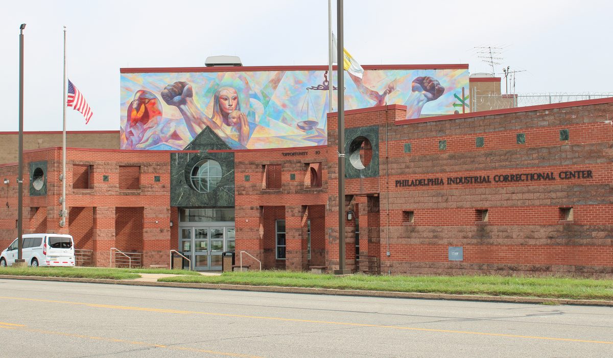 Front entrance of the Philadelphia Industrial Correctional Center (PICC). Above the entrance, the facade features a painted mural. A white municipal van is parked just past the doors.